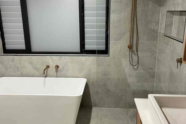 A modern bathroom in Epping, NSW, featuring a freestanding bathtub, rain shower, and sleek gray tiles.