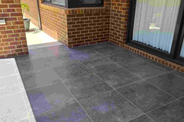 A tiled outdoor patio repaired in Cheltenham NSW, featuring large gray tiles and brick walls.